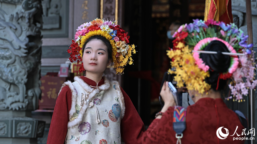 簪花的姑娘在蟳埔庙埕前留影，一袭红妆配簪花围，定格闽南习俗的灵动瞬间。人民网记者 李昌乾摄