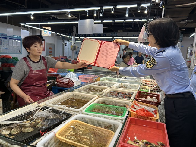 工作人員向商家介紹《水產市場誠信計量管理規范》